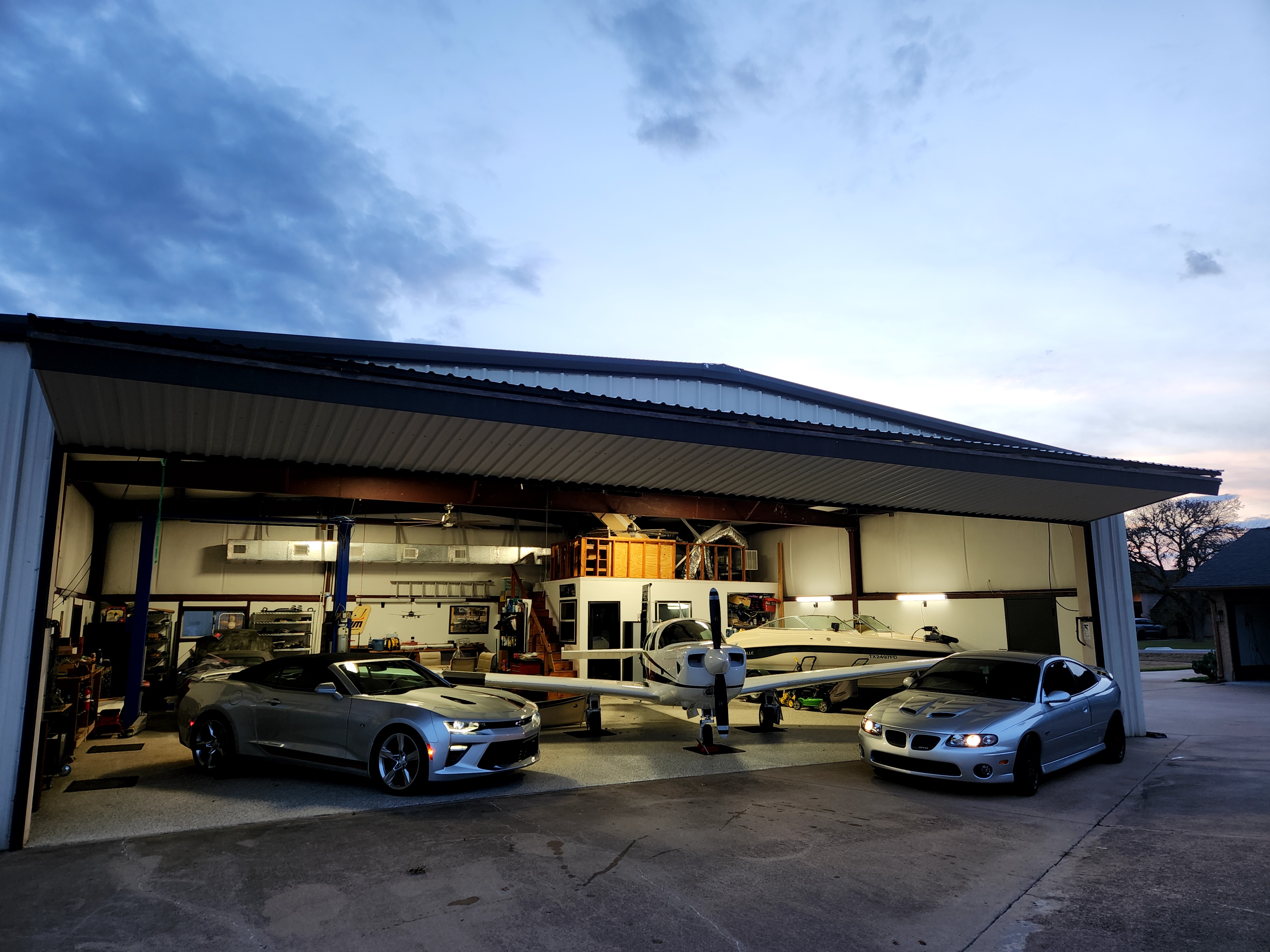 Hangar at blue hour with cars and plane glowing inside against dramatic sky
