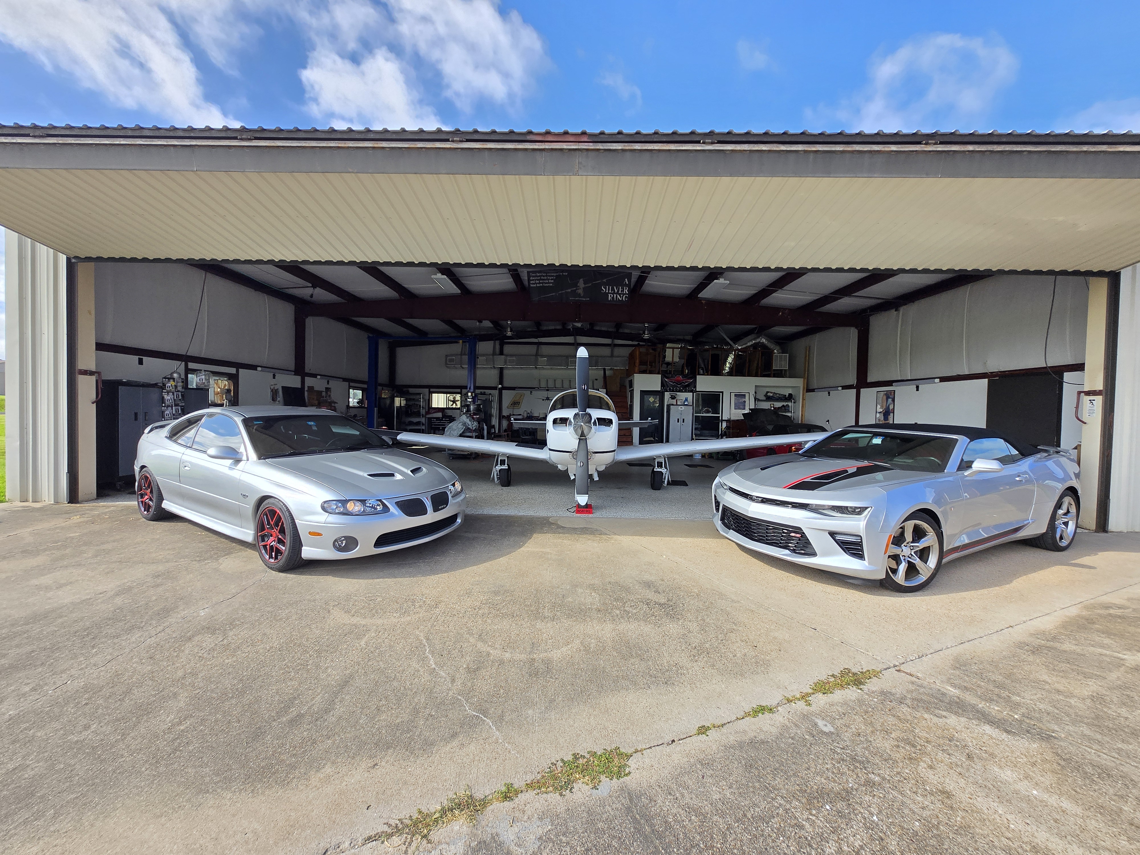 Hangar exterior daytime with GTO and Camaro convertible flanking Mooney