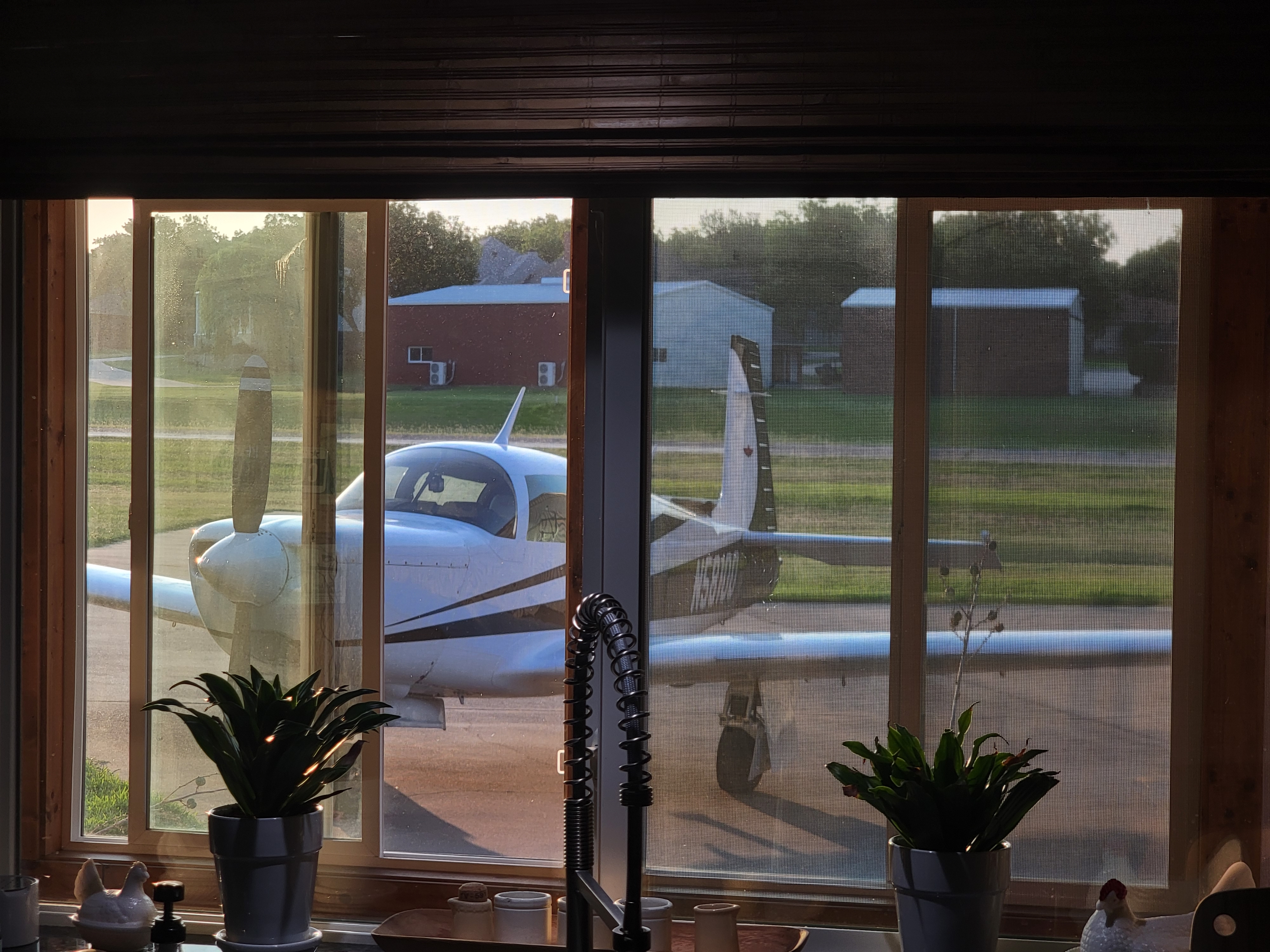 Mooney parked on the ramp viewed through kitchen window at golden hour