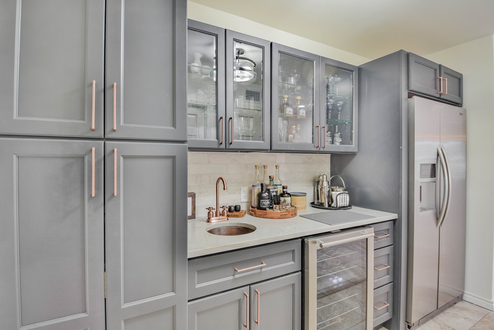 Wet bar with gray cabinets, rose gold hardware, copper round sink, wine cooler